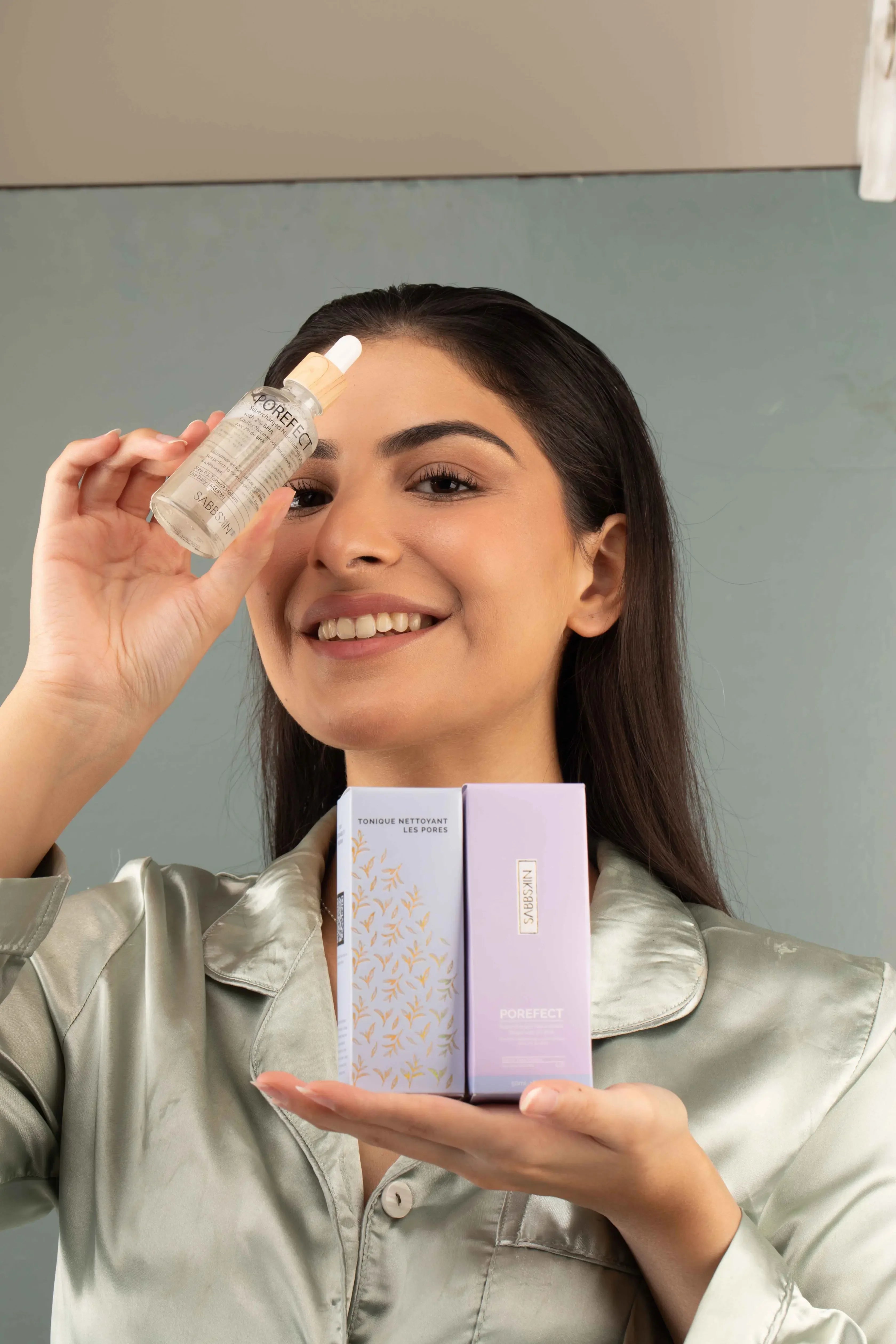 Woman smiling and holding Sabe Skin Porefect serum and skincare product boxes