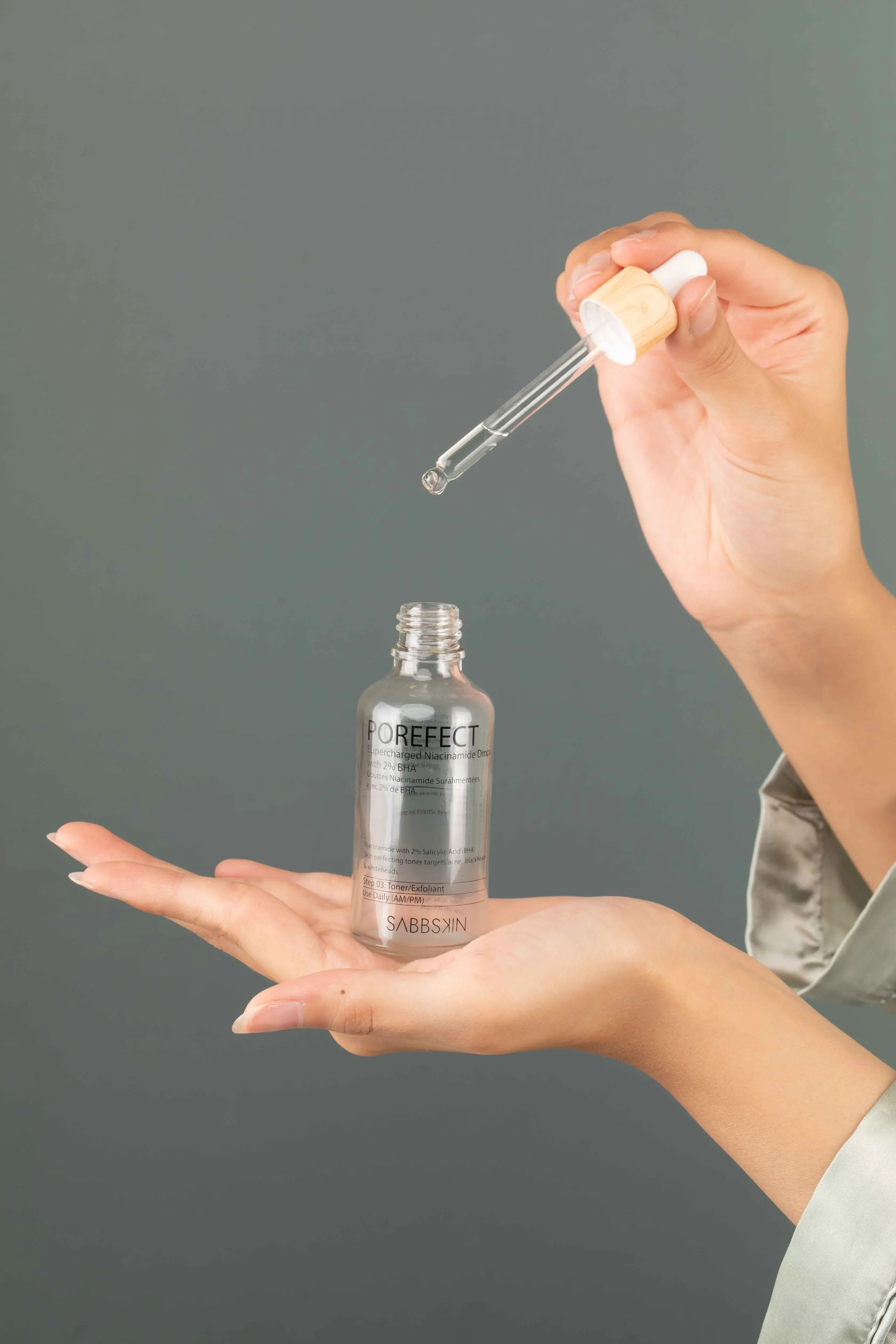 Hand holding Sabbskin Porefect Niacinamide serum dropper bottle against gray background